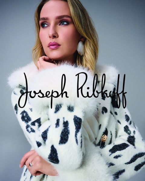Una donna con un cappotto di pelliccia sintetica bianca a pois neri posa pensierosa. Il nome "Joseph Ribkoff" è scritto in nero sopra l'immagine.