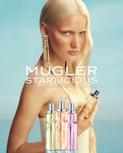 Una donna con lunghi capelli biondi tiene in mano una boccetta di profumo. Nella parte inferiore dell'immagine, si vedono tre boccette colorate "Mugler Starlcious" davanti a un cielo blu.