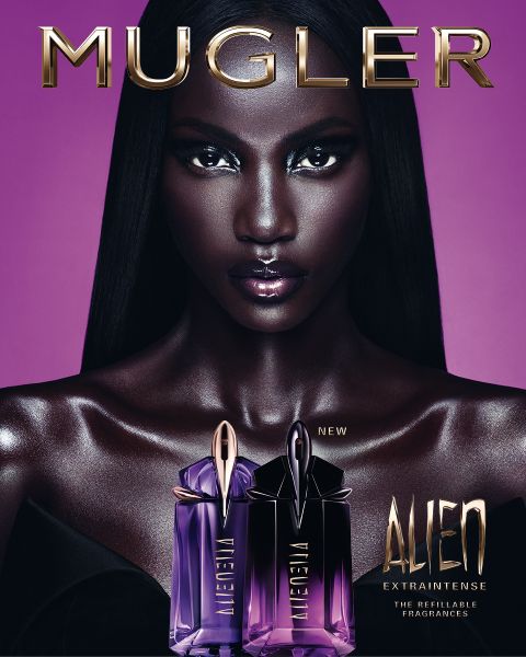 Una donna con una pelle scura e radiosa e lisci capelli neri posa davanti a uno sfondo viola. Davanti a lei ci sono due flaconi di profumo Alien di Mugler. Il testo recita "MUGLER" e "ALIEN EXTRA INTENSE LE FRAGRANZE RICARICABILI".