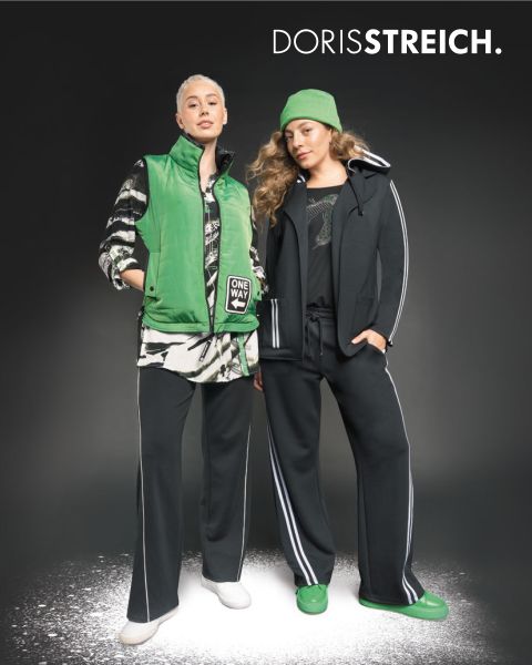 Due donne posano con sicurezza in abiti in bianco e nero con accenti verdi, tra cui un gilet imbottito, un cappello e scarpe, davanti a uno sfondo scuro con il testo "DORIS STREICH" sopra di loro.
