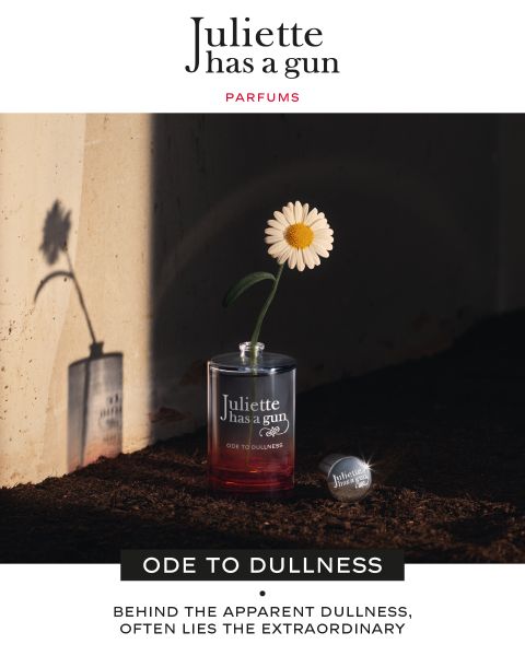 Su una mensola c'è un flacone di profumo trasparente in vetro con le scritte "Juliette has a gun" e "ODE TO DULLNESS". All'interno del flacone c'è una singola margherita bianca. L'ombra della margherita si proietta su una parete retrostante. La luce del sole crea un effetto drammatico.