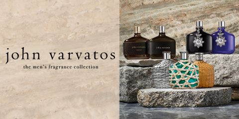 Una selezione di sei fragranze maschili di John Varvatos esposte su lastre di pietra. I flaconi variano nel design e nel colore, da motivi intrecciati a superfici lisce e metalliche. Il testo a sinistra recita "John Varvatos, la collezione di fragranze maschili".