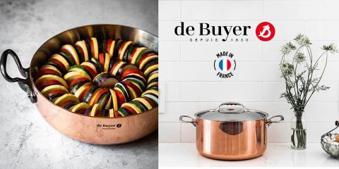 Una pentola di rame piena di strati di zucchine, melanzane e fette di pomodoro. Accanto c'è una casseruola di rame con coperchio davanti a una parete piastrellata di bianco con fiori in un vaso. Il logo di de Buyer e il testo "Made in France" sono visibili.