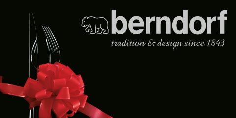 Un set di posate, composto da forchetta, coltello e cucchiaio, è legato insieme con un nastro rosso. Il testo recita "berndorf tradition & design since 1843", con un logo stilizzato di un orso sopra "berndorf". Lo sfondo è nero.