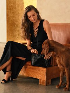 Una donna in abito nero è seduta con un cane marrone su un divano marrone e tiene una borsa nera in grembo.