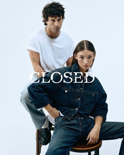 Un uomo in maglietta bianca e jeans è seduto su una sedia di legno, rivolto in avanti. Una donna in giacca di jeans e jeans è seduta di fronte a lui, leggermente reclinata. Entrambi hanno un'espressione seria. Sopra l'immagine c'è la parola "CHIUSO".