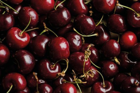 Un primo piano di numerose ciliegie rosse mature con gambi verdi. Le ciliegie hanno una lucentezza brillante che indica freschezza. Alcuni gambi sono visibili e creano un contrasto con le ricche tonalità rosse del frutto.