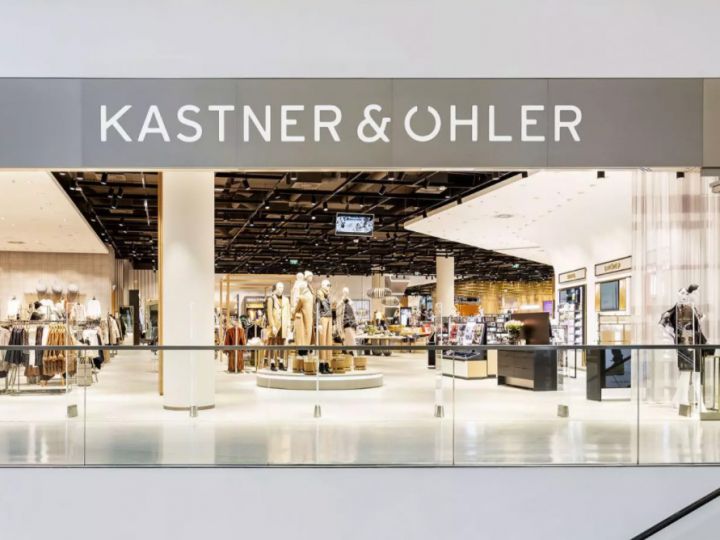 La facciata del negozio di Kastner & Öhler mostra un moderno interno di un grande magazzino con manichini che espongono abbigliamento. Il nome del negozio è ben visibile su un'insegna chiara e moderna sopra l'ingresso.