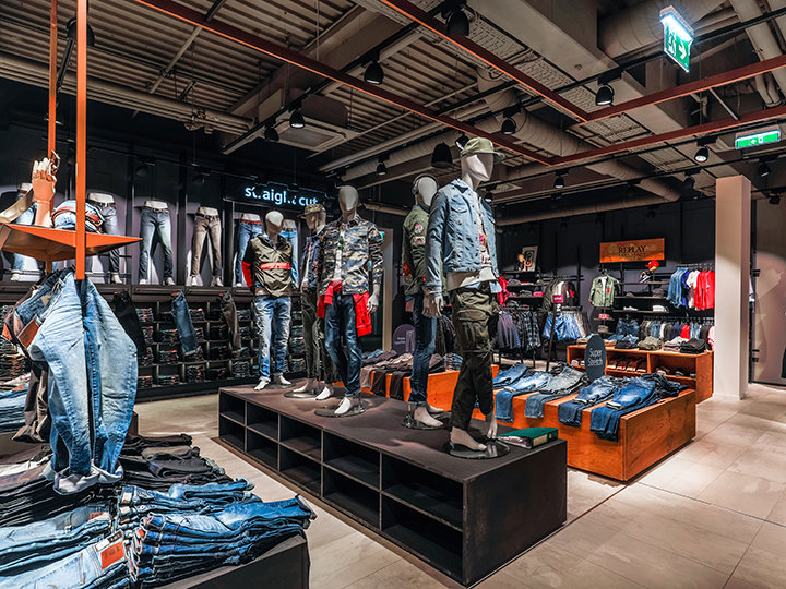 Un negozio di abbigliamento alla moda con manichini vestiti in modo casual, tra cui jeans e giacche. Scaffali e stand espongono una varietà di capi in denim sotto una luce intensa, creando un'atmosfera moderna ed elegante.