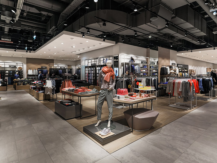 Un moderno negozio di abbigliamento con manichini eleganti che espongono abbigliamento da donna. Il negozio presenta scaffali e ripiani ben organizzati con una varietà di vestiti e accessori, e un'illuminazione brillante valorizza lo spazio.