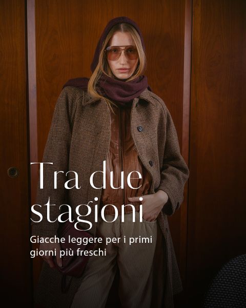 Una donna in un outfit autunnale a strati con occhiali da sole e sciarpa in piedi davanti a un rivestimento in legno; il testo recita: "Tra due stagioni, Giacche leggere per i primi giorni più freschi.".