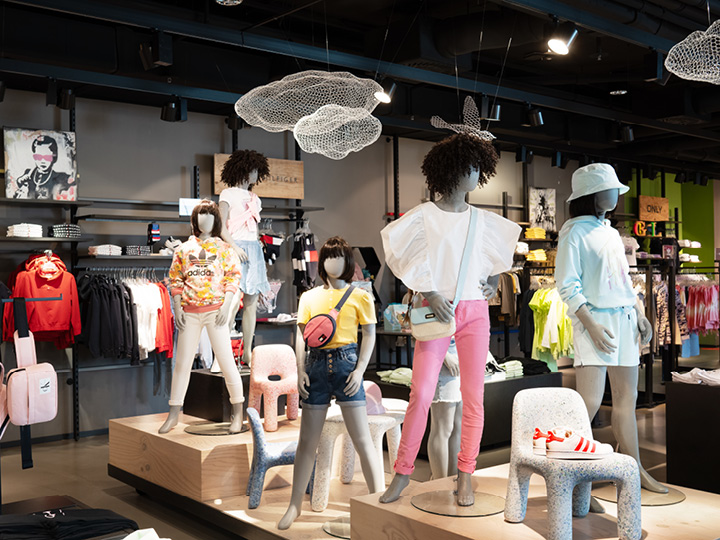 In un negozio di abbigliamento alla moda, i manichini espongono abiti casual colorati. Il negozio offre una varietà di capi di abbigliamento e accessori su uno sfondo elegante e moderno con elementi decorativi artistici appesi al soffitto.