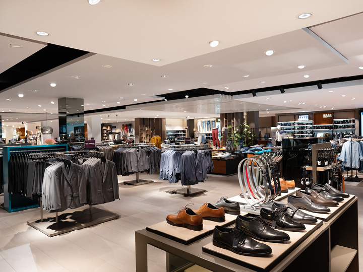 Un interno spazioso di un negozio di abbigliamento con abiti ordinatamente disposti su stand, scarpe eleganti su un tavolo espositivo e accessori come cinture. Il negozio è ben illuminato e arredato in stile moderno, creando un'atmosfera di shopping di lusso.