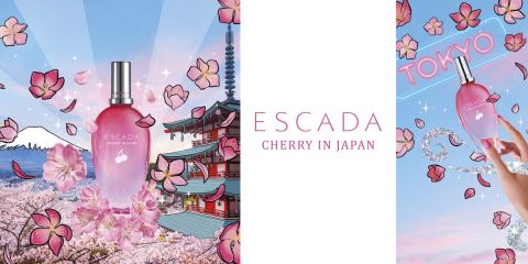 Una bottiglia della fragranza "Cherry in Japan" di Escada si trova di fronte a uno sfondo vivace di ispirazione giapponese con fiori di ciliegio, un tempio e la Tokyo Tower. Il cielo è illuminato da raggi e petali in stile cartone animato fluttuano intorno. La parola "TOKYO" appare al neon.