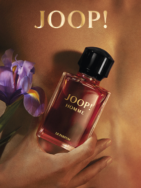 Una bottiglia di JOOP! Homme Le Parfum è tenuta davanti a uno sfondo sfocato con un fiore di iris viola. Il logo dorato di "JOOP!" è chiaramente visibile in alto. L'immagine trasmette eleganza e lusso.