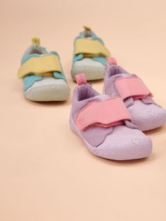 Due paia di scarpe per bambini su sfondo beige: un paio è viola chiaro con cinturini rosa, l'altro è azzurro con cinturini gialli.