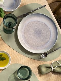 Apparecchiatura della tavola con una tovaglietta verde, un piatto di ceramica, un bicchiere, una forchetta, un coltello, una piccola ciotola con olio e aneto e un tovagliolo di stoffa verde con anello portatovagliolo.
