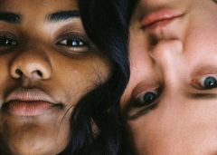 Nahaufnahme von zwei Personen mit unterschiedlichem Hautton, die ihre Köpfe dicht aneinander legen. Eine Person ist aufrecht und die andere kopfüber. Beide haben einen neutralen Ausdruck, der die Details ihrer Gesichter einfängt.