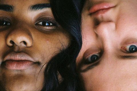 Primo piano di due persone con diverse tonalità della pelle che avvicinano le teste. Una persona è in posizione verticale e l'altra a testa in giù. Entrambe hanno un'espressione neutra che cattura i dettagli dei loro volti.