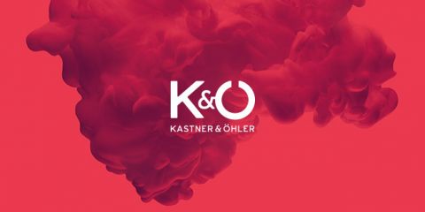 Ein roter Hintergrund mit wirbelndem Rauch oder Tinte und dem weißen Logotext „K & Ö“ über „Kastner & Öhler“ in der Mitte.