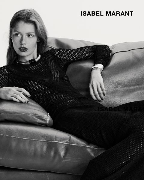 Una donna è sdraiata su un divano di pelle e indossa un abito nero a maniche lunghe e strutturato. L'immagine è in bianco e nero, con la scritta "ISABEL MARANT" in grassetto nell'angolo in alto a destra e in basso.