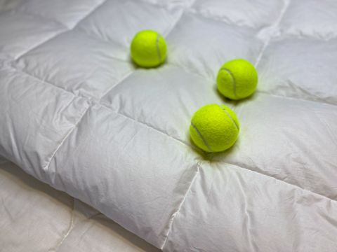 Tre palline da tennis verde neon giacciono su una soffice trapunta bianca, creando un contrasto morbido e accogliente.