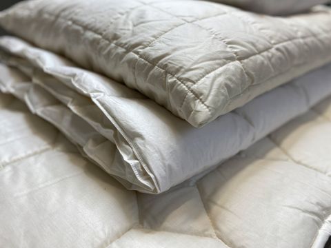 Un primo piano di coperte bianche trapuntate, piegate ordinatamente e impilate su una superficie. Il tessuto appare morbido e soffice, trasmettendo calore e comfort.