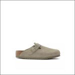 Ein einzelner taupefarbener Wildleder-Slipper mit Schnallenriemen oben, Korkfußbett und flacher Gummisohle, dargestellt auf einem schlichten weißen Hintergrund.