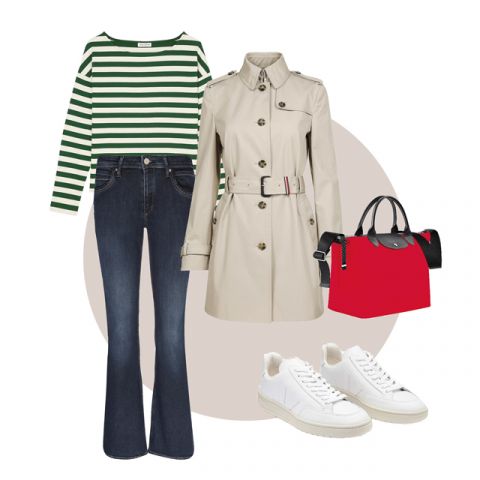 Un outfit elegante composto da una maglia a maniche lunghe a righe verdi e bianche, un trench beige, jeans a zampa blu scuro, sneakers bianche e una borsa rossa con dettagli neri. L'ensemble è disposto su uno sfondo neutro.