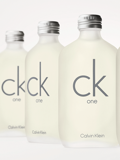 Quattro flaconi opachi di Calvin Klein CK One sono visibili su uno sfondo chiaro. I flaconi presentano la scritta grigia "ck one" e tappi argentati.