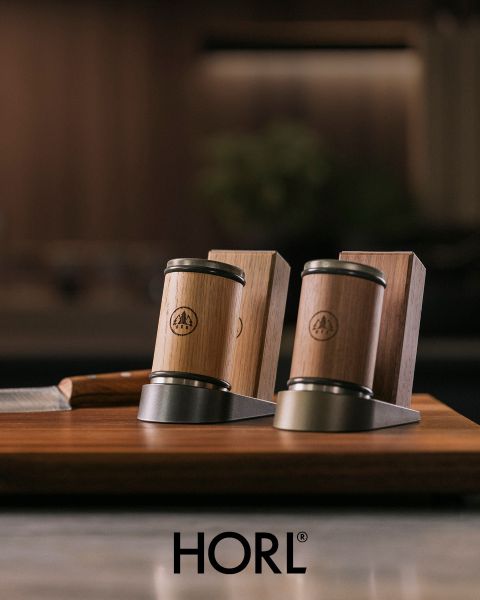 Due affilacoltelli in legno e metallo e un portacoltelli in legno su una base di legno, sotto con il logo "HORL".