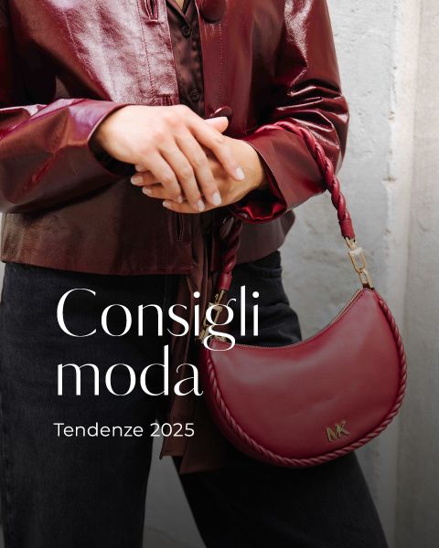 Una persona con una lucida giacca di pelle color borgogna tiene in mano una borsetta MK color borgogna abbinata. Il testo sull'immagine recita: "Consigli moda Tendenze 2025.
