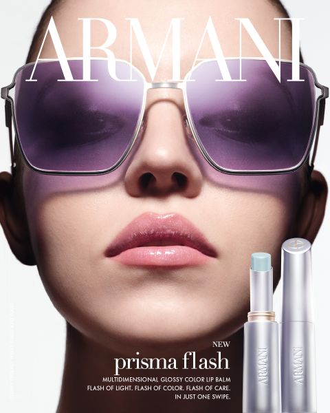 Primo piano di una donna con occhiali da sole oversize e labbra rosa lucide, con in basso a destra visibili due balsami labbra Armani Prisma Flash.