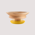 Eine runde, flache Holzschale mit breitem Rand, platziert auf einem kleinen, glänzend gelben Sockel. Die Schale hat ein modernes Design und steht vor einem schlichten, hellgrauen Hintergrund.
