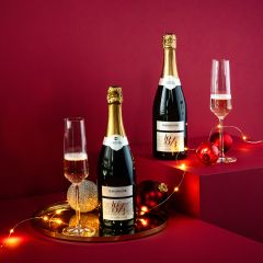 Zwei Champagnerflaschen mit gefüllten Gläsern, platziert auf einem roten Hintergrund mit festlichen Lichterketten und Ornamenten. Die Szene ist auf erhöhten Plattformen aufgebaut und schafft eine festliche und elegante Atmosphäre.