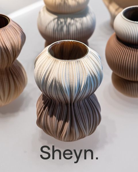 Un vaso scultoreo in ceramica con una struttura ondulata in tonalità neutre, tra cui la scritta in grassetto Sheyn".