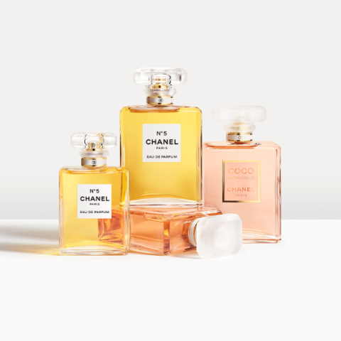 Quattro flaconi di profumo Chanel, tra cui due No. 5 Eau de Parfum con liquido dorato e due Coco Mademoiselle, sono disposti su una superficie bianca. I profumi si trovano in eleganti flaconi di vetro con tappi squadrati che proiettano ombre delicate.