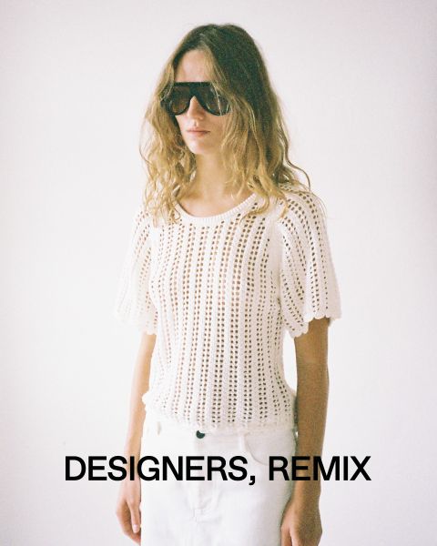 Una persona con i capelli lunghi, grandi occhiali da sole e un top bianco all'uncinetto è in piedi davanti a uno sfondo semplice. Nella parte inferiore dell'immagine ci sono le parole "Designers, Remix".