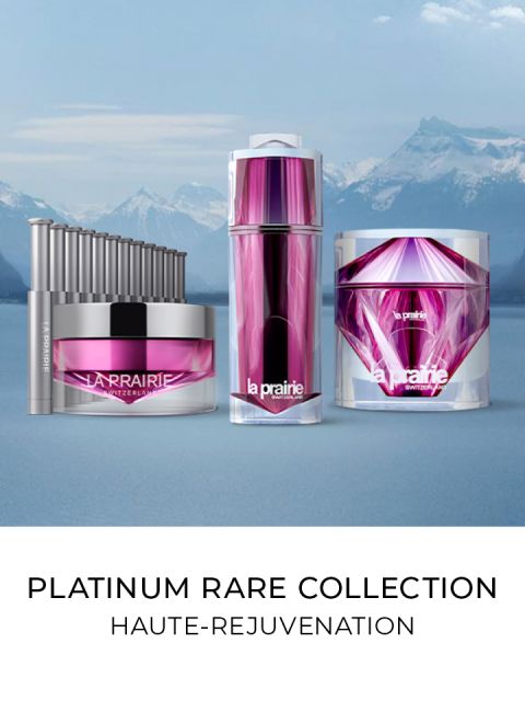 Una collezione di prodotti per la cura della pelle Platinum Rare di La Prairie, tra cui una crema, un siero e un applicatore. Hanno un'elegante confezione viola e argento, sullo sfondo di montagne innevate e un lago. Testo: "Platinum Rare Collection, Haute-Rejuvenation".