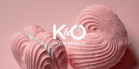 Zwei rosa Baisers in Herzform auf einem zartrosa Hintergrund. Der Text „K & Ö KASTNER & ÖHLER“ ist deutlich über dem Bild zu sehen.