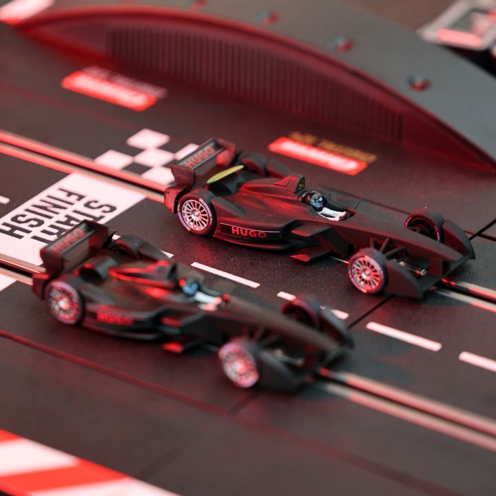 Due auto da corsa modello su una pista per slot car con una linea di partenza/arrivo a scacchi. Le auto sono eleganti e scure, e la pista ha accenti rossi. Sullo sfondo si vede un cavalcavia curvo.