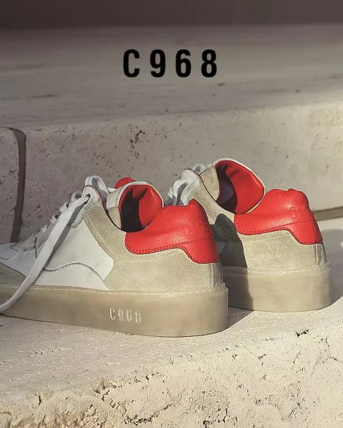 Un paio di sneaker alla moda su una superficie di pietra. Hanno tomaie bianche e grigie con audaci accenti rossi sul tallone. Il numero "C968" appare sul gradino sullo sfondo e sulle suole delle scarpe.