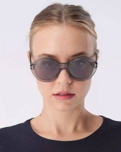 Una persona con occhiali da sole rotondi neri e una camicia nera guarda avanti su uno sfondo bianco semplice. I capelli sono pettinati all'indietro.