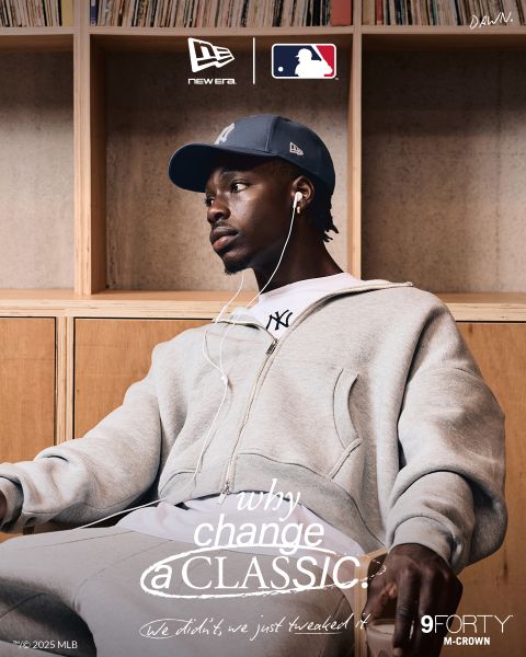 Un uomo che indossa una tuta grigia, una t-shirt bianca e un cappellino blu scuro dei New York Yankees è seduto su una panchina di legno e ascolta musica con delle cuffie bianche. Il testo pubblicizza il cappellino 9FORTY M-Crown di New Era con il marchio MLB.