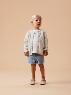 Una giovane ragazza sorridente in tuta color lavanda posa su uno sfondo grigio con un grande fiocco bianco in testa.