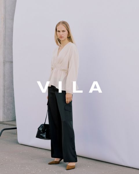 Cinque donne in abbigliamento casual, tra cui jeans e top in colori neutri, sono in piedi vicine e sorridono davanti a uno sfondo semplice. Il testo sovrapposto recita "Vila Clothes".