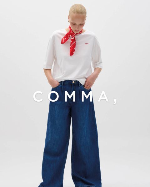 Una donna con un cappotto a quadri e accessori dorati posa con un cane marrone chiaro e bianco in un abito a quadri abbinato. La parola "COMMA" appare in grande carattere bianco su tutta l'immagine.