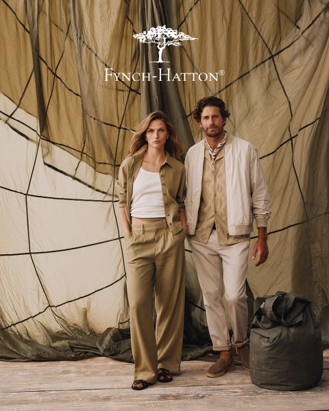 Un uomo con capelli castani ondulati e barba indossa un maglione blu navy e si trova di fronte a una parete beige strutturata. Il logo e il nome di Fynch-Hatton appaiono nell'angolo in alto a destra.