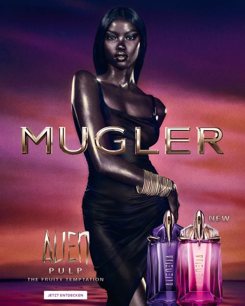 Una donna con una pelle scura e radiosa e lisci capelli neri posa davanti a uno sfondo viola. Davanti a lei ci sono due flaconi di profumo Alien di Mugler. Il testo recita "MUGLER" e "ALIEN EXTRA INTENSE LE FRAGRANZE RICARICABILI".