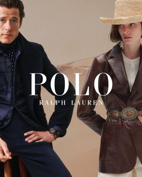 Un uomo e una donna indossano eleganti trench Ralph Lauren. L'uomo abbina il suo cappotto a un maglione colorato e pantaloni grigi, mentre la donna indossa una camicia a righe, guanti marroni e una cintura larga. "POLO RALPH LAUREN" è mostrato in caratteri bianchi.